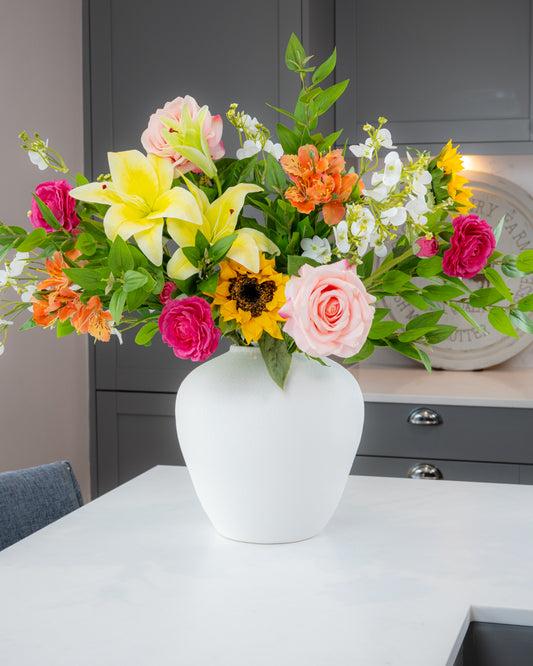 Colorful bouquet of flowers in a white vase on a table with a neutral background