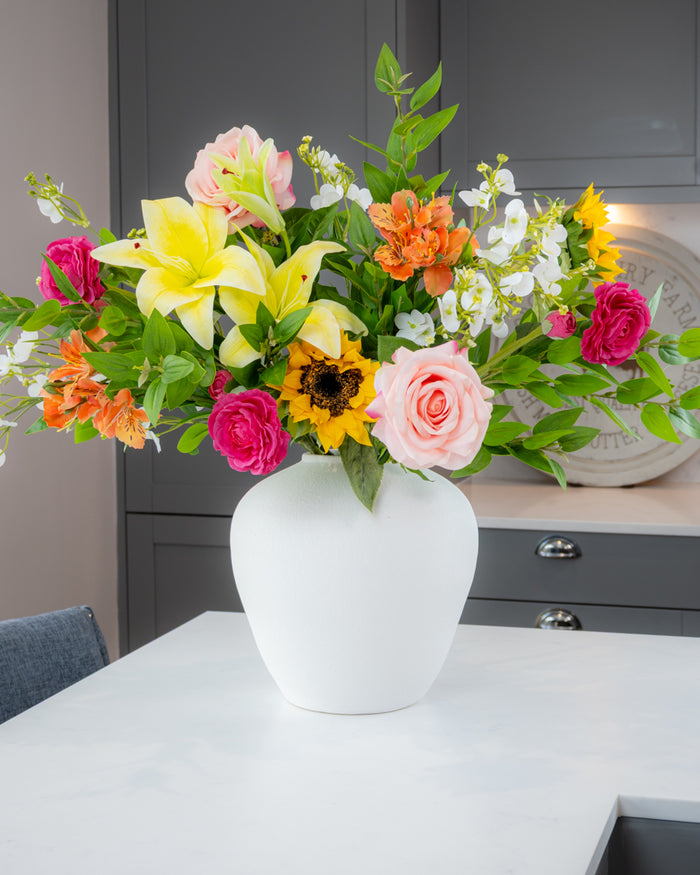 Colorful bouquet of flowers in a white vase on a table with a neutral background